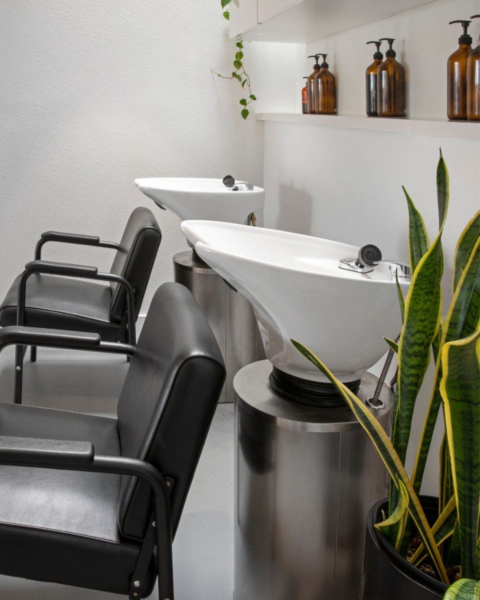 two white shampoo sinks on stainless steel pedestals with black shampoo chairs