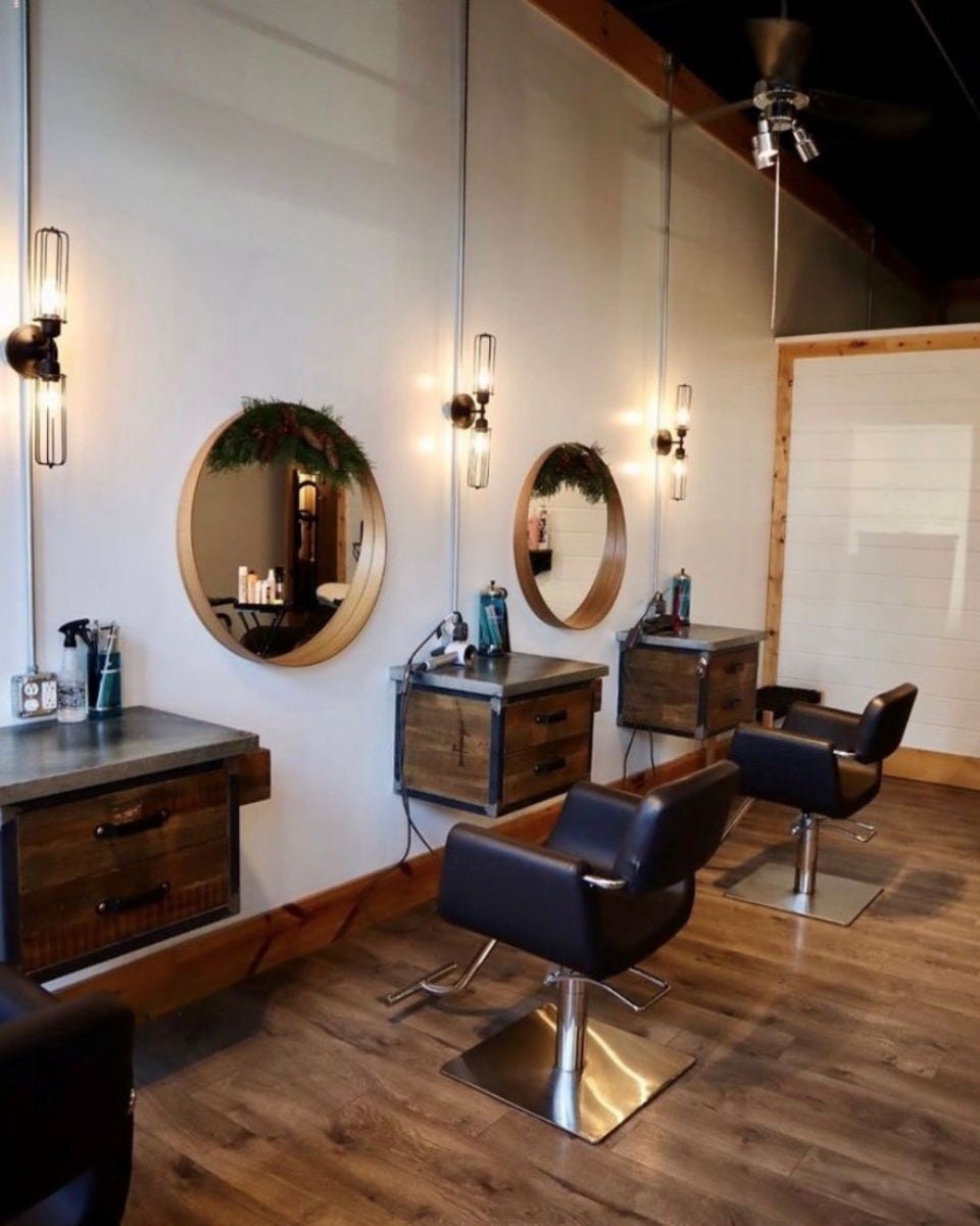 three wall-mounted styling stations with hammered zinc countertop, spacious drawers and hand-sculpted iron frames in a modern hair salon with industrial decor