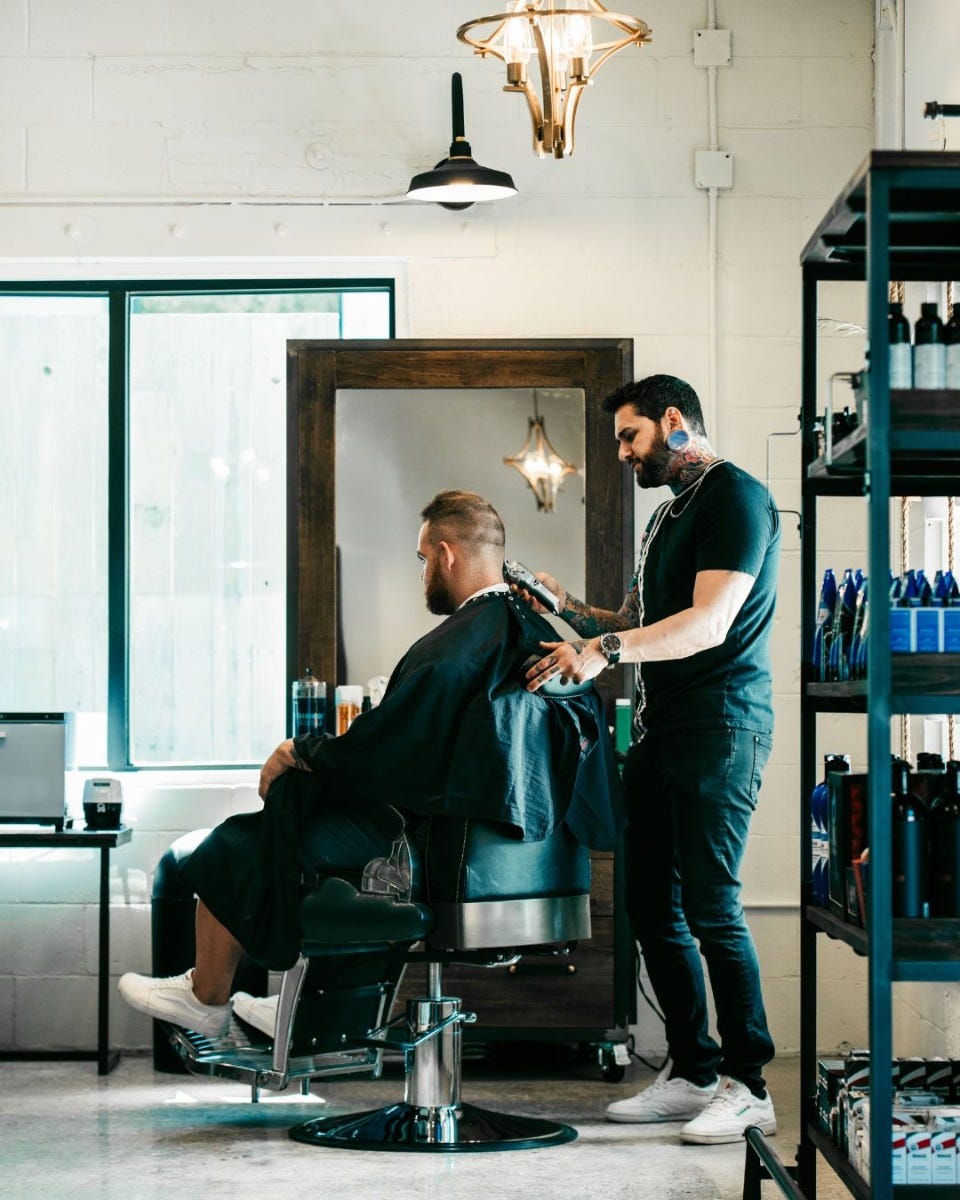 barber using clippers on a tall client in a height-adjustable barber chair