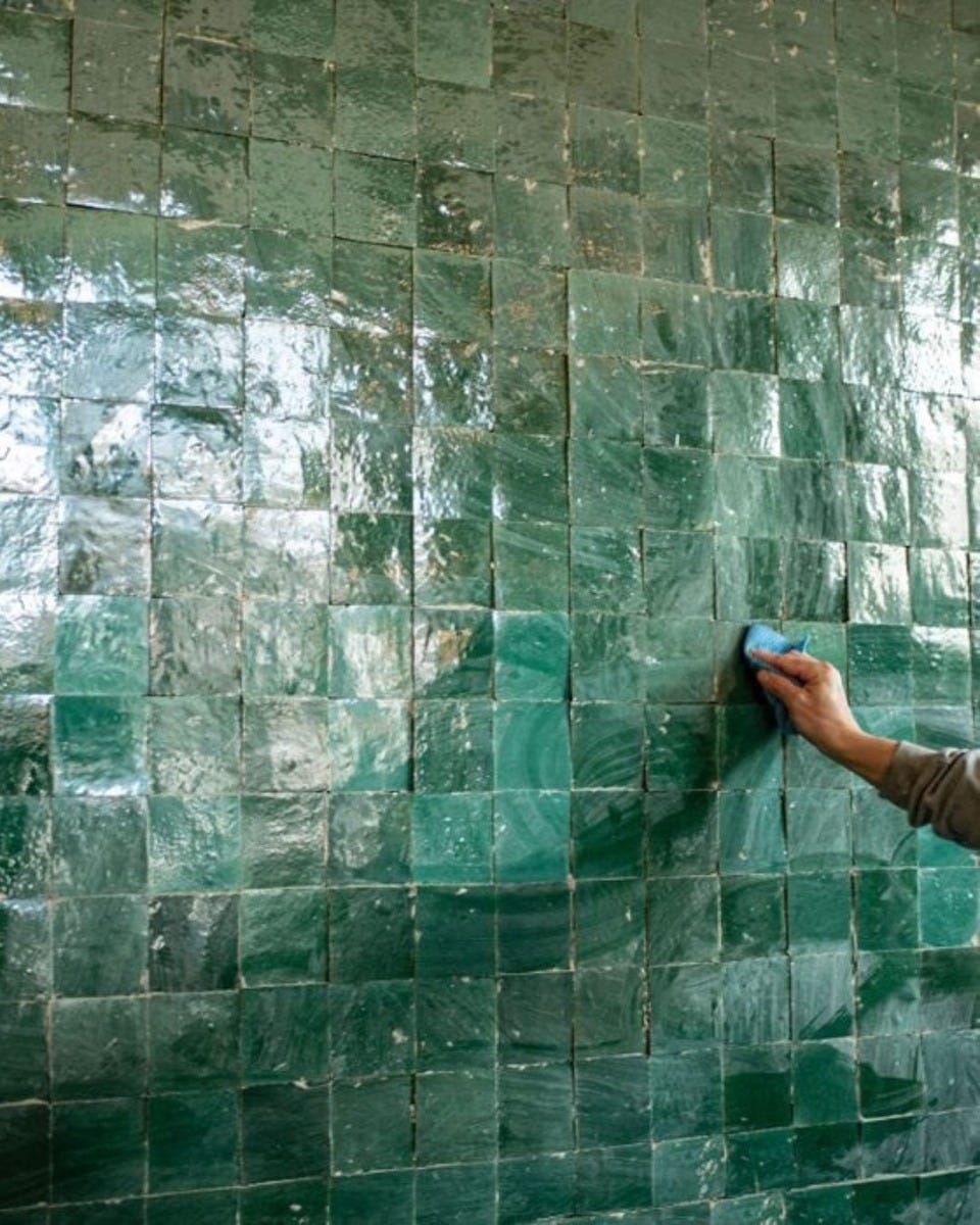 teal tiled wall being cleaned by hand holding a blue sponge