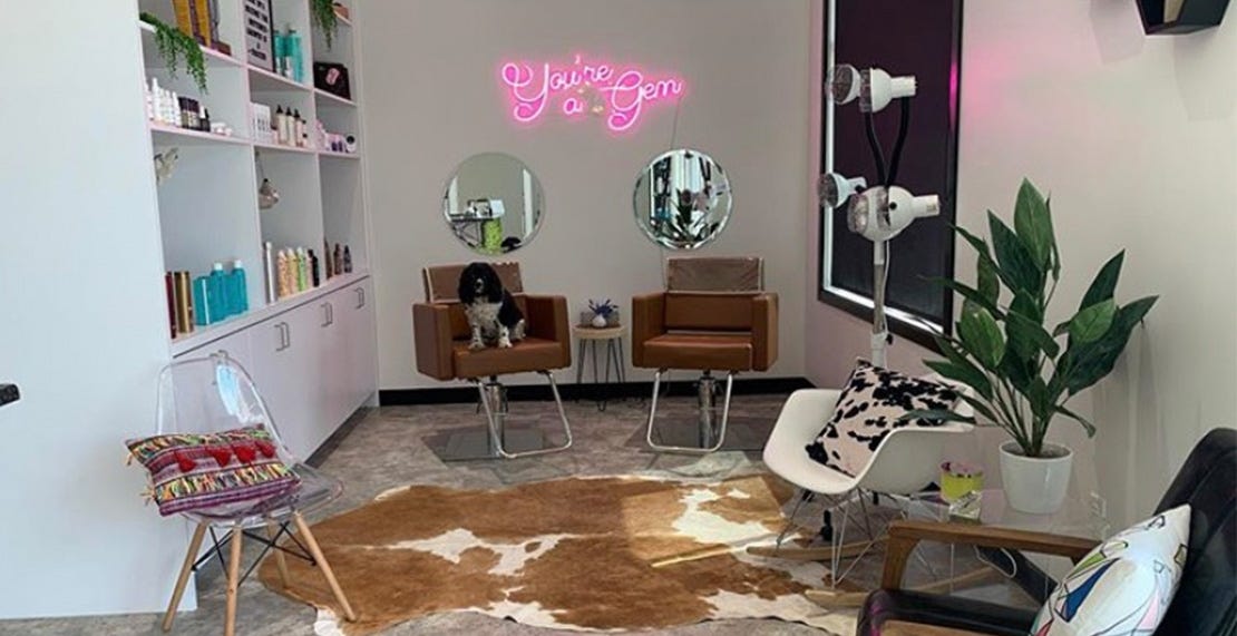 small salon suite with storage shelving, styling chairs and neon sign