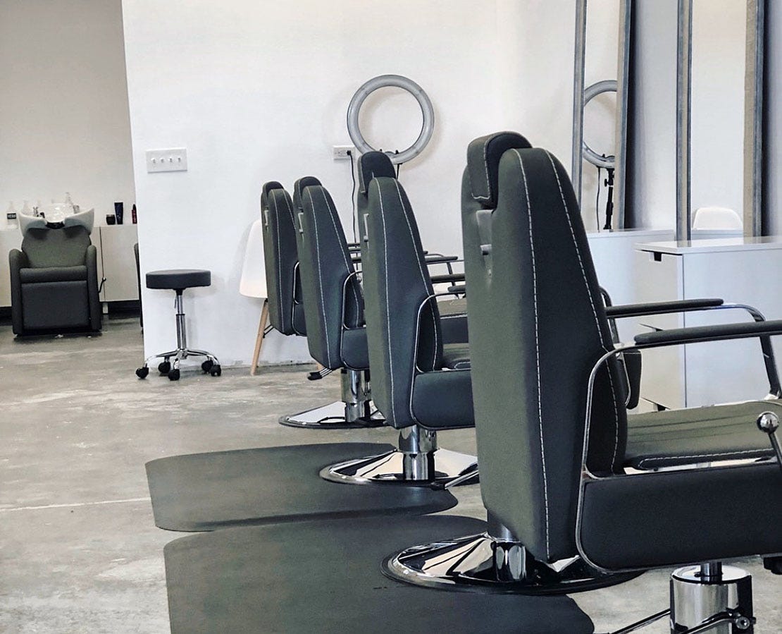 white barber styling stations with full length mirrors, black barber chairs and a wash station in the background